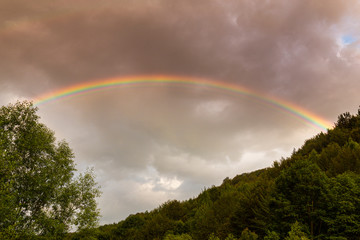 Rainbow profiled on storm clouds, in the mountais