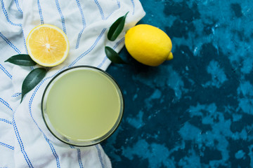  A glass of lemon juice and fresh lemons on a blue background. Top view. Copy space.