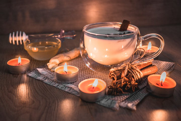 Glass cup of traditional indian masala chai tea lit by candlelight. Indian masala chai tea - spiced tea with milk on rustic wooden background, selective focus, copy space. Close up.