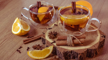 Orange flavored tea with cinnamon and cardamom in glasses, orange and cinnamon sticks on a wooden table. Mulled wine and spices on wooden background. Selective focus. Close up.