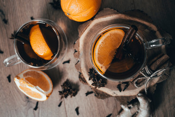 Fototapeta na wymiar Orange flavored tea with cinnamon and cardamom in glasses, orange and cinnamon sticks on a wooden table. Mulled wine and spices on wooden background. Selective focus. Close up.
