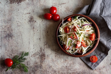 Appetizing vegetarian salad with cabbage, tomatoes, herbs, olive oil in a stylish plate on a gray background