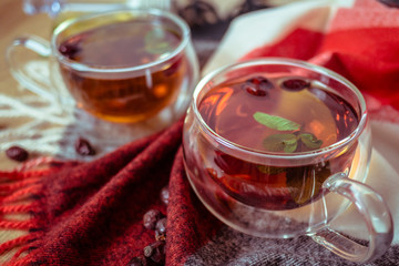 Dried rose-hip berries and rosehip tea on the rustic table. In a glass cups tea of rosehip and leaves mint. Medicinal plants and herbs composition. Autumn and winter season background. Close up