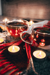 Black cup tea with dried rosehip and fresh leaves mint on the background of scattered dried rose hips and wax candles. Selective focus. Close up. Autumn and winter background.
