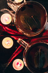 Black cup tea with dried rosehip and fresh leaves mint on the background of scattered dried rose hips and wax candles. Selective focus. Close up. Autumn and winter background.