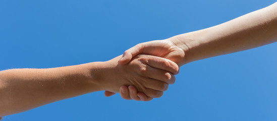 Helping hand concept. Gesture, a sign of help and hope. Two hands take each other. Against the background of blue sky banner.