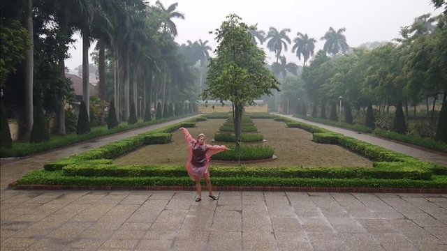 A girl is dancing in a red raincoat in the rain in a park in Hanoi