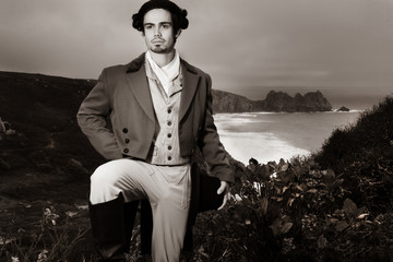 Portrait of handsome 18th century gentleman dressed in vintage costume, holding top hat with ocean...