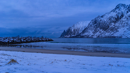 plage et bord de mer enneigés avec des montagnes pointues sur l'ile de senja à l'heure bleue avec des couleurs magenta