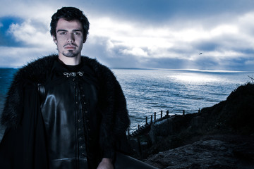 Portrait of handsome knight with goatee and fur coat looking at camera with ocean in background