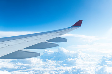 Obraz premium View from the airplane window on clouds, blue clear sky. Look seen through window of an aircraft. Wing of a flying airplane. Good sunny weather.