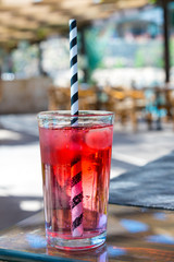 Red cocktail with ice with a straw on a on bar background. vertical photo