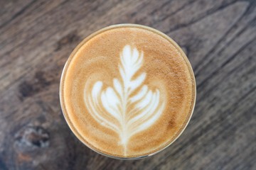 Glass of hot coffee with beautiful latte art on wooden table, top view