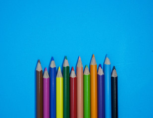 Crayons and pastels lined up isolated on blue paper background with copy space