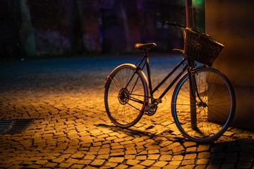 Fototapeta na wymiar a bicycle lashed to a pole on a city street, lit by a lamp at night