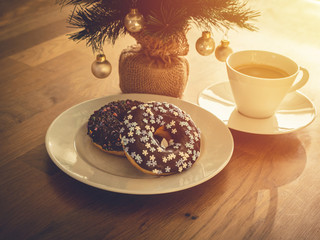 Chocolate donuts sprinkled with colorful stars on the table. Coffee and Christmas decorations in the background. Donut on Christmas table. Chocolate donut at sunrise. Coffee and donut.