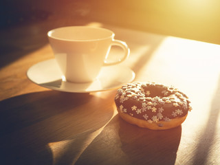 Chocolate donuts sprinkled with colorful stars on the table. Coffee decorations in the background. Donut on table. Chocolate donut at sunrise. Coffee and donut.
