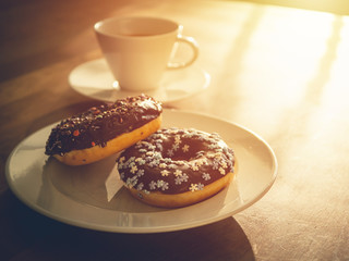 Chocolate donuts sprinkled with colorful stars on the table. Coffee decorations in the background. Donut on table. Chocolate donut at sunrise. Coffee and donut.