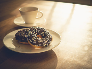 Chocolate donuts sprinkled with colorful stars on the table. Coffee decorations in the background. Donut on table. Chocolate donut at sunrise. Coffee and donut.