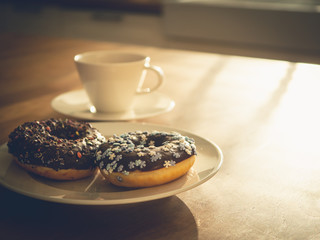 Chocolate donuts sprinkled with colorful stars on the table. Coffee decorations in the background. Donut on table. Chocolate donut at sunrise. Coffee and donut.