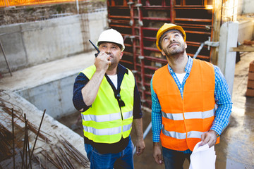 Men in hardhat and yellow and orange jacket posing on building site