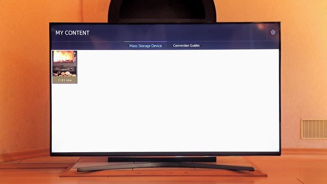 Television with the video of the burning stove stands before the stove in the apartment. The TV screen imitates the fire in the fireplace stove.