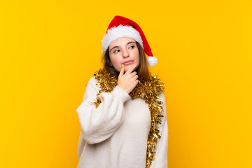 Girl with christmas hat over isolated yellow background thinking an idea
