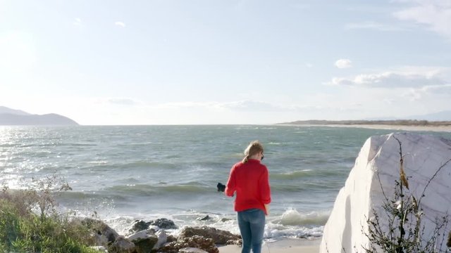 Woman with red knitted sweater and DSLR camera taking pictures on the beach, slow motion.