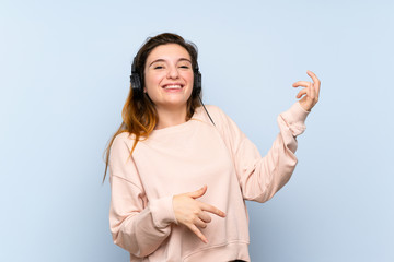 Fototapeta premium Young brunette girl over isolated blue background using the mobile with headphones and dancing