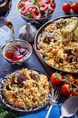 Uzbek pilaf in an authentic blue and gold dish, shot on a blue background with tomatoes, garlic and tea