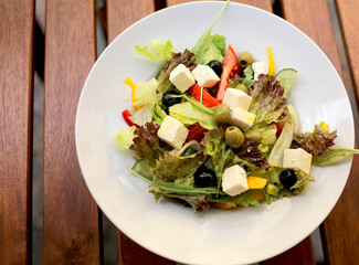 Greek salad (lettuce, tomatoes, feta cheese, cucumbers, black olives) on a dark wooden background top view