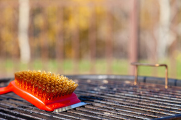 Close-up of a red brush with golden bristles and a scraper for cleaning a barbecue grill grate. The...