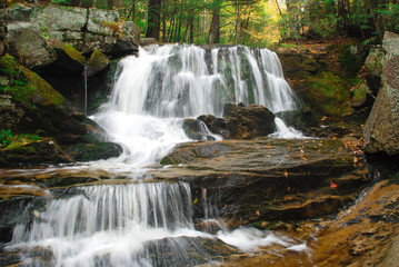 Obraz premium Kaskadowy wodospad z gładką wodą płynącą w lesie jesienią