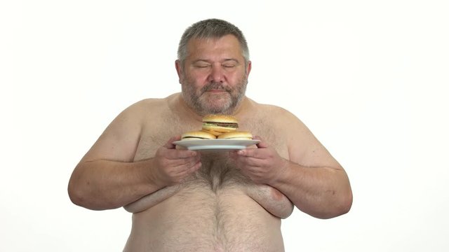 Fat man enjoying smell of burgers. Overweight man holding plate with junk food over white background. Bad eating habits.