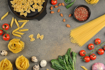 Pasta and ingredients for making pasta sauce. Spinach, spices, garlic, quail eggs, cherry tomatoes, almonds, parmesan cheese on a dark background. Free space for text. View from above.