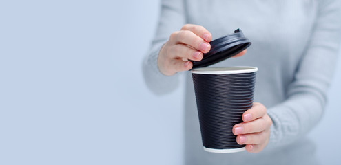 Woman holding cardboard cup of coffee in hand on gray light background