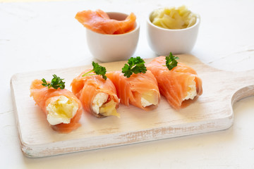 Slices of smoked salmon wrapped with cottage cheese and marinated ginger. Party snack.