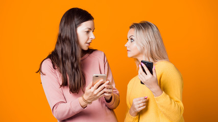 Two cheerful friends communicate and show each other something in phones, live communication, modern technologies.