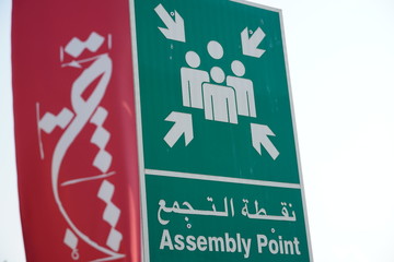 Dubai UAE - November 2019: Emergency assembly point information sign in white paint on green background fixed to a pole to direct people where to go in case of an emergency.