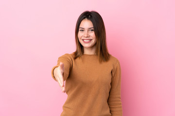 Fototapeta premium Young woman over isolated pink background shaking hands for closing a good deal