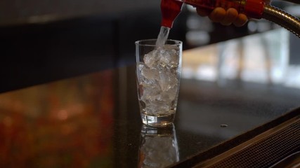 Man using a soda gun to pour clear pop into a soda glass in a restaurant bar.