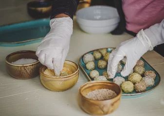 Foto op Canvas Hands preparing plant based energy balls with coconut flakes and sesame seed toppings on platter © Cristina
