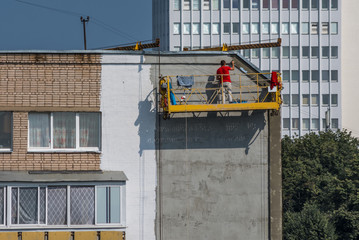 Worker plasterer on a crane repair the facade of a old panel concrete house