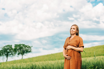 Outdoor portrait of stylish pregnant woman, wearing brown dress