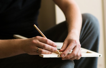 young man doing carpenter's job, measures a piece of wood and uses a pencil