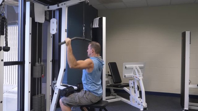 Man at the gym exercising, working out strength training, doing lat pulldowns on a lat pull down exercise machine.