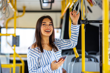 Smiling young woman traveling by bus and using smart phone. Sweet girl with sunglasses in using phone while standing in a bus. A young woman travelling by bus and looking at her smart phone © Dragana Gordic