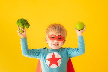 Superhero child holding broccoli and apple