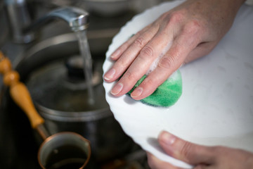 a woman washes dishes with a foam sponge