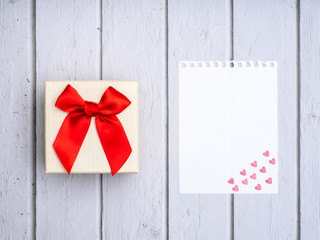 Flat lay yellow box with red bow and and   and white sheet of paper with little pink hearts on White wooden table Wedding card ideas and Valentines Day copy space for text